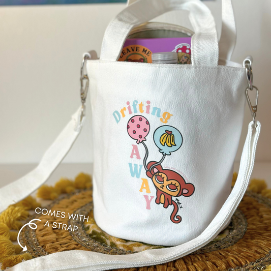 White tote bag with a monkey design and text 'Drifting Away' on a woven canvas bucket bag