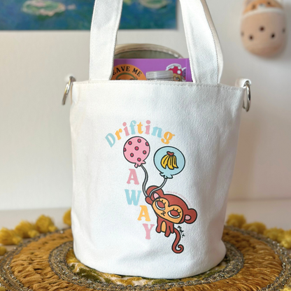 White tote bag with a colorful monkey design and text on a textured surface.