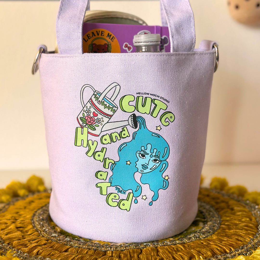 purple tote bag with cartoon character and text 'Cute and Hydrated' on a yellow textured surface.
